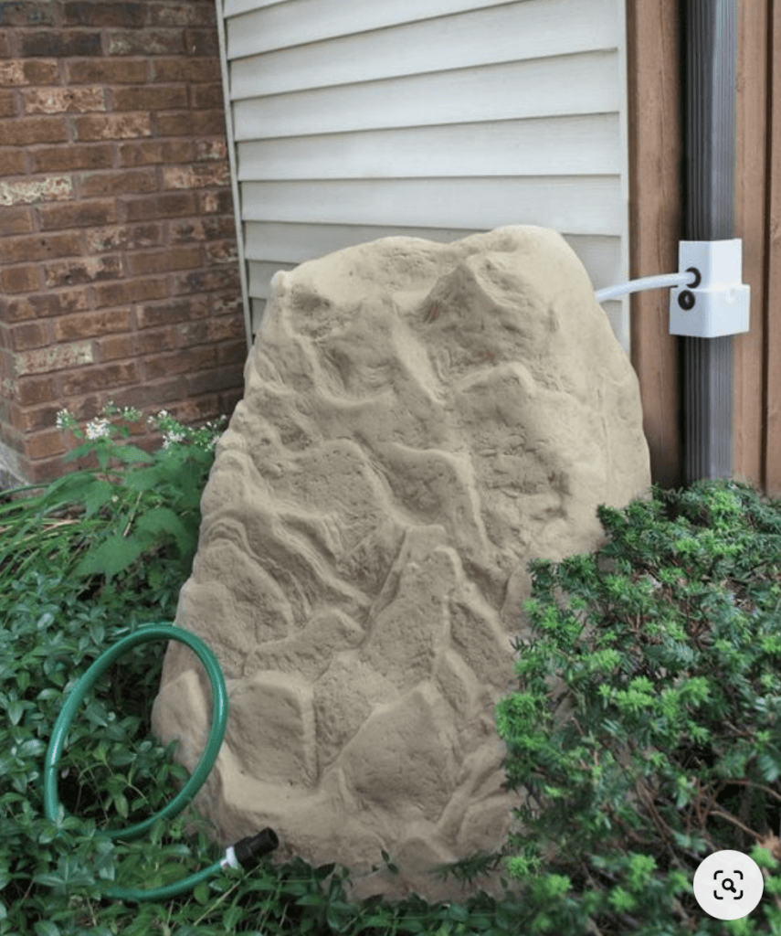 fake rock that surrounds a small rain barrels hooked up to a house